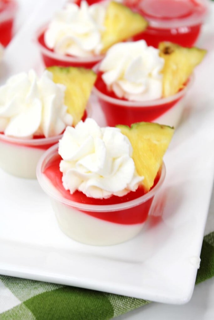 close up of shots showing whipped cream and pineapple piece on top 