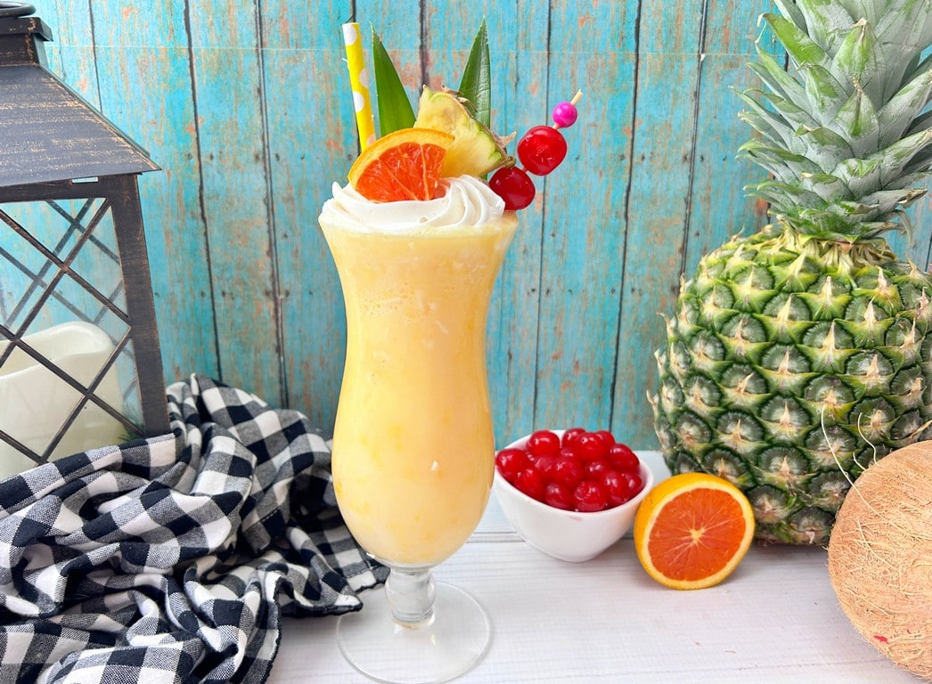 cocktail with white bowl full of cherries, full pineapple and orange slice beside. 