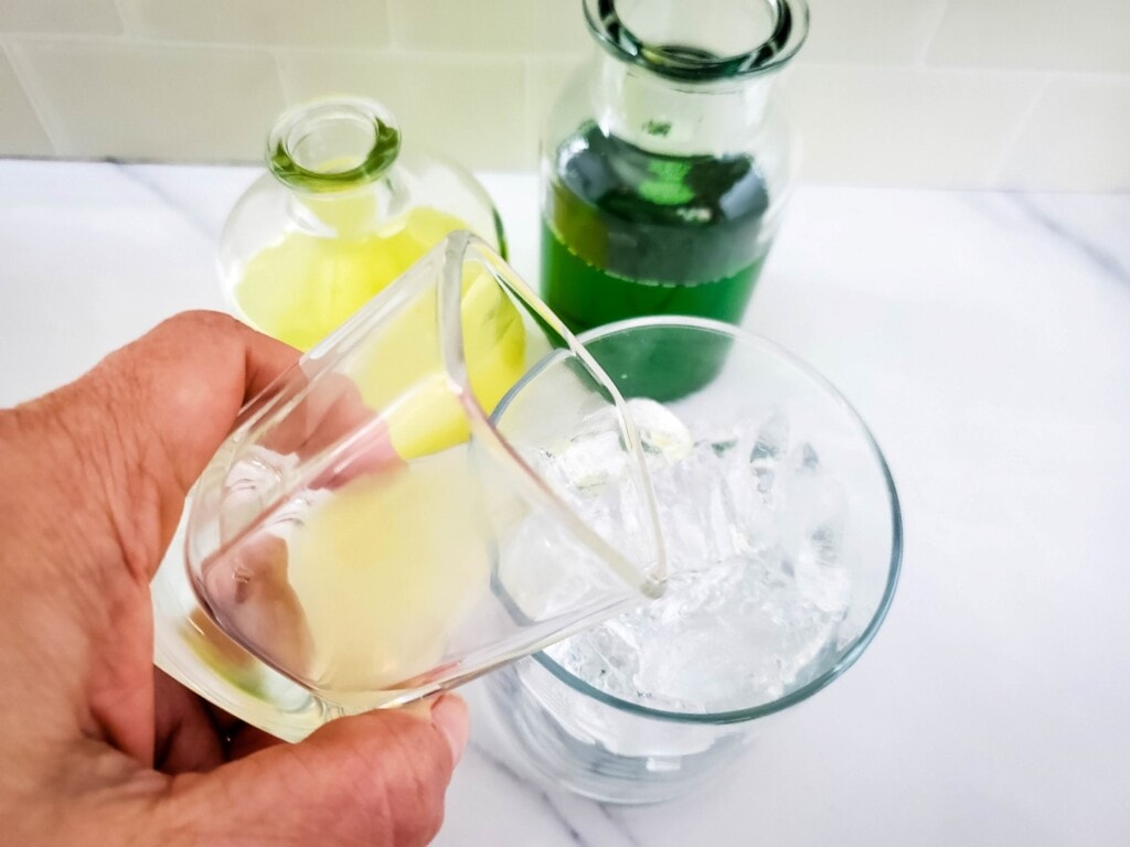 Pouring lime juice into glass with ice and tequila in it. 