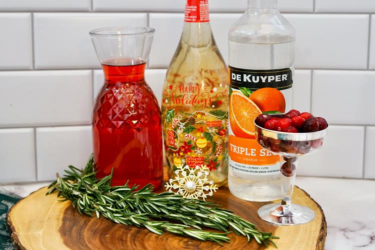 Ingredients needed: cranberry juice, champagne, triple sec, glass of cranberries, and fresh rosemary. 