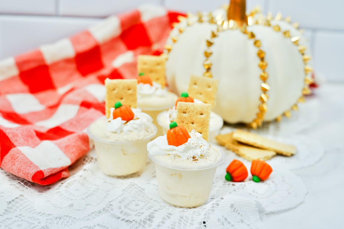Pumpkin Spice Pudding Shots - white pudding shot with whipped cream, spices, pumpkin candy, and graham cracker sticking out. 