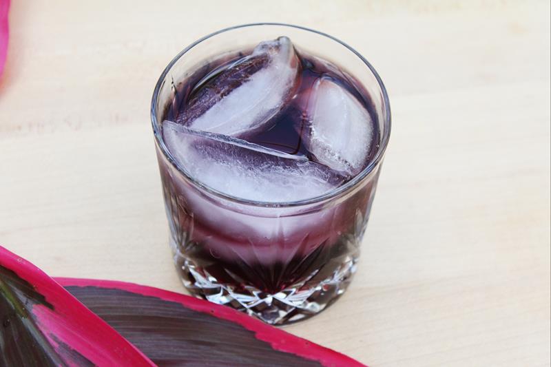 close up of cocktail showing three large ice cubes and dark purple drink 