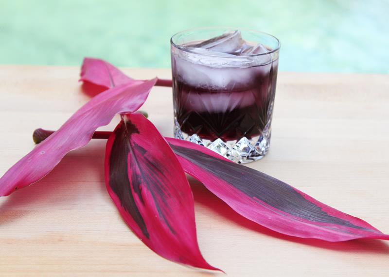 showing completed cocktail with ice and purple plant leaves beside it 