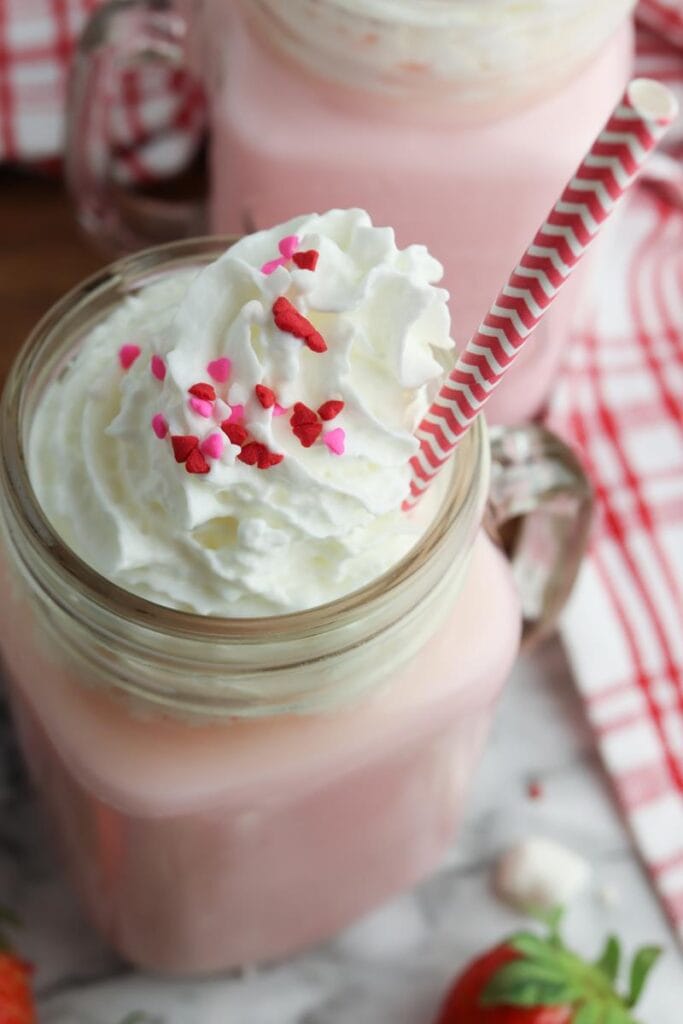 closer up of strawberry hot chocolate with shipped cream and heart sprinkles 