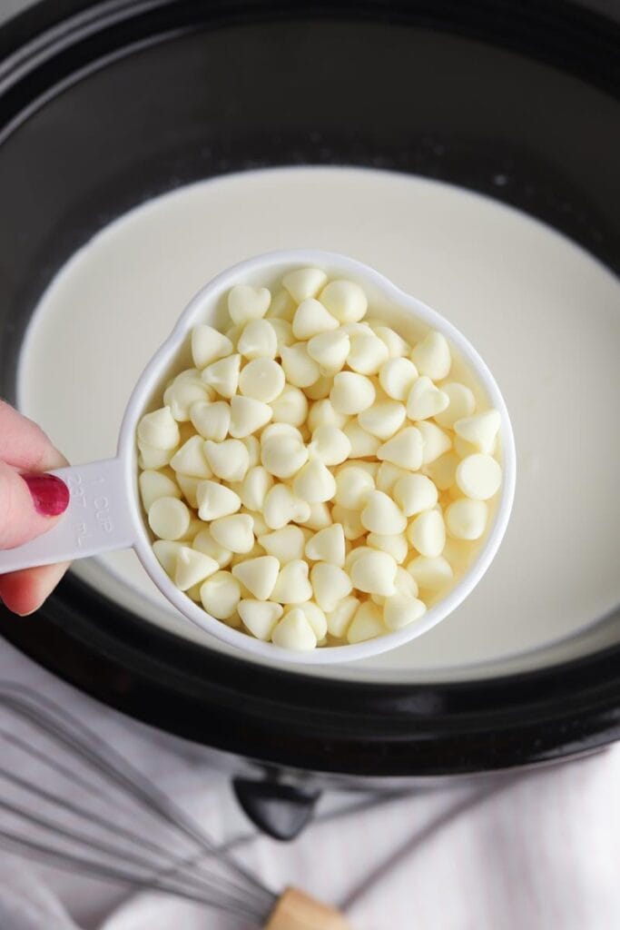 cup of white chocolate chips above slow cooker with cream and mik in it 