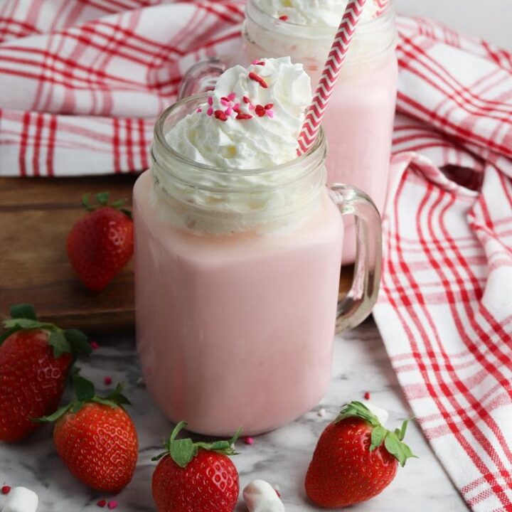 strawberry hot chocolate in clear tall glass with strawberries around it
