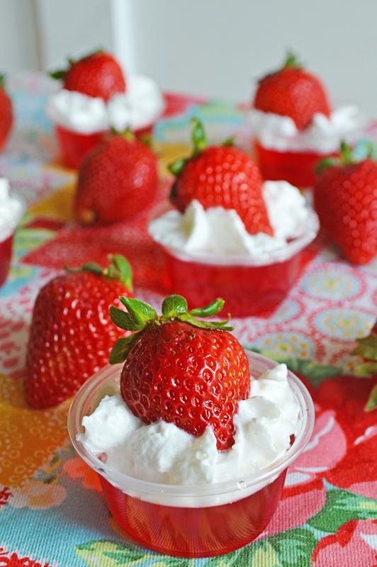 closer up photo of strawberry jello shot with whipped cream and full strawberry 