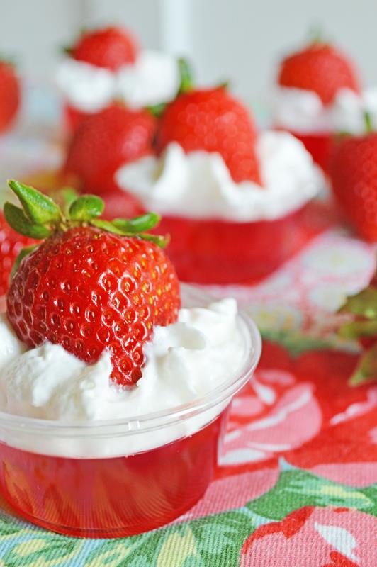 close up photo of strawberry jello shot with whipped cream and full strawberry 