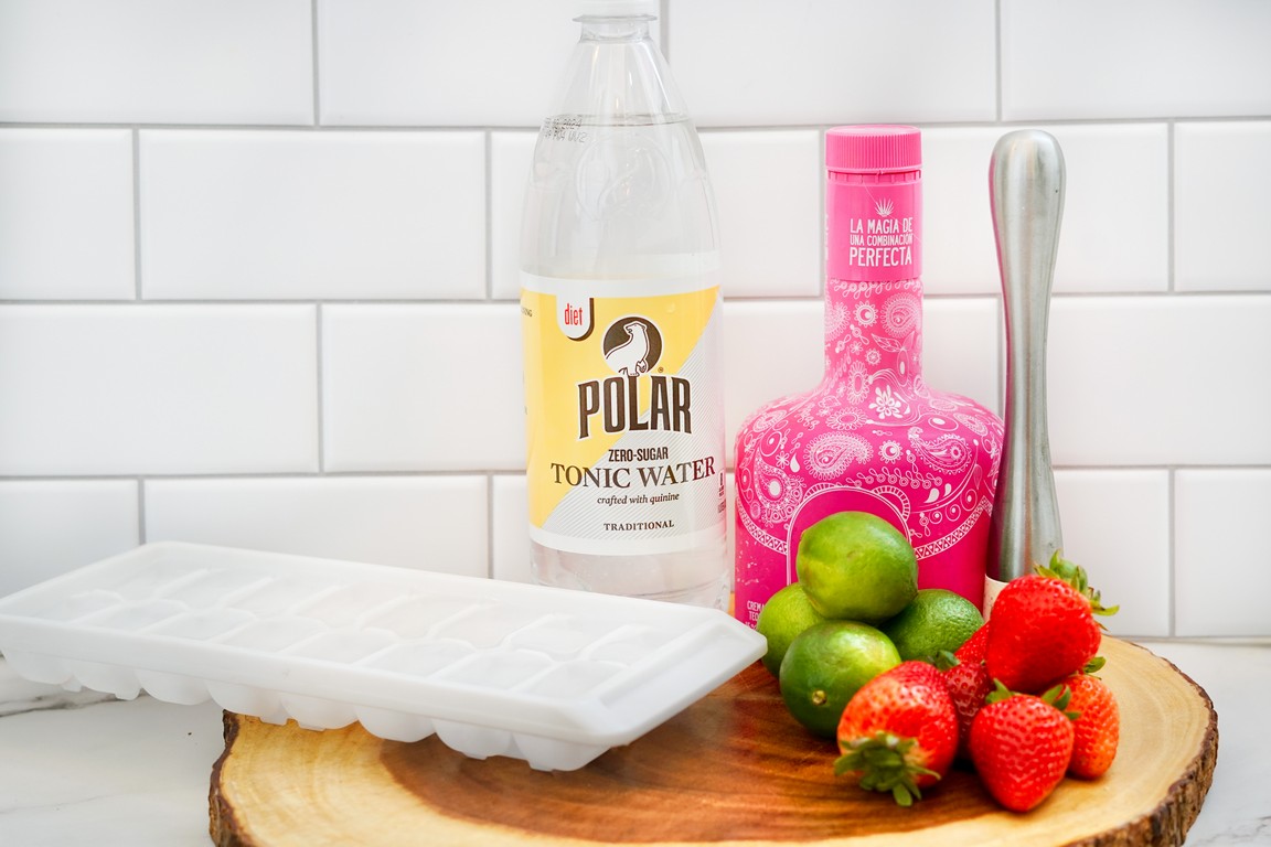 Ingredients required for Strawberry Tequila soda : Ice cube tray, tonic water bottle, pink tequila bottles, muddler, full limes, and fresh strawberries. 