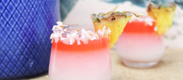 shot glass rimmed with coconut and a small slice of pineapple. Shot is dark pink on top and fades to white.