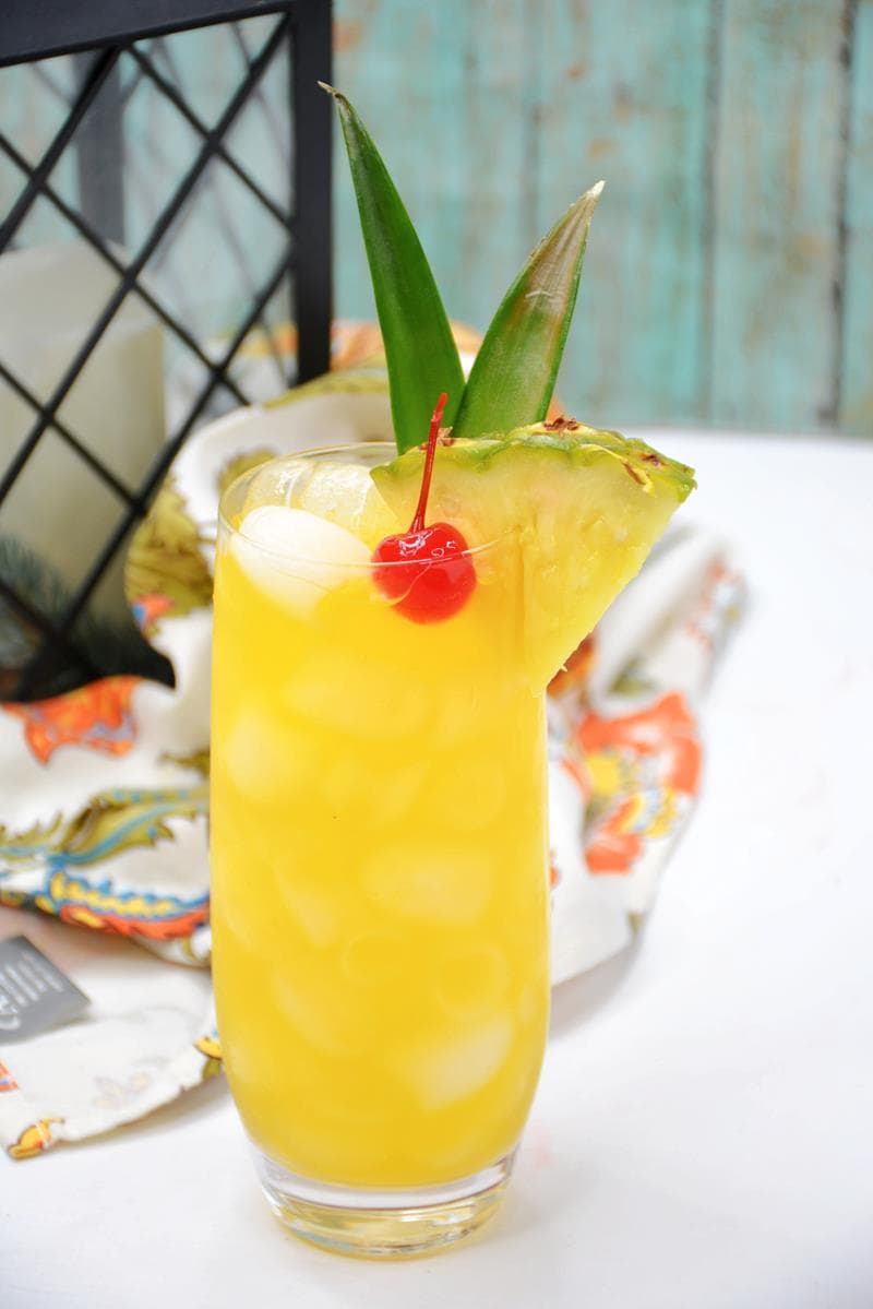whisky sour drink with one charry, ice, pineapple wedge and pineapple crown sticking out of it 