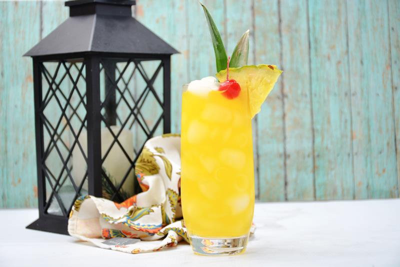 tropical whisky sour with cherries, ice, and pineapple wedge in front of an outdoor candle lamp