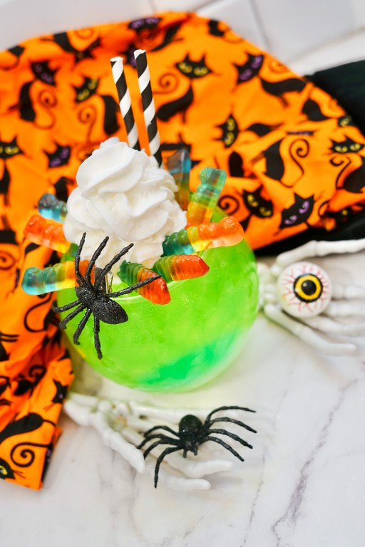 Wiggly Worm Halloween Mocktail: Green and blue mocktail with a fake black spider, whipped cream, and gummy worms as garnish. 