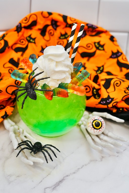 Wiggly Worm Halloween Mocktail in front of a orange cloth with black cats all over it. 