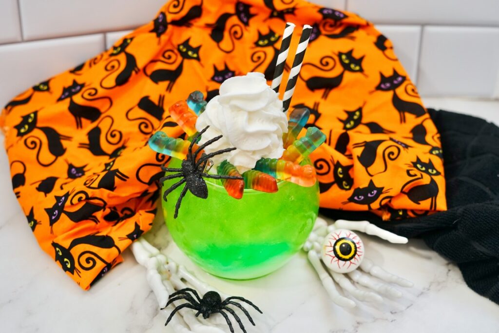 completed mocktail with fake skeleton hands, eyeballs, and black spiderrs all around it. 