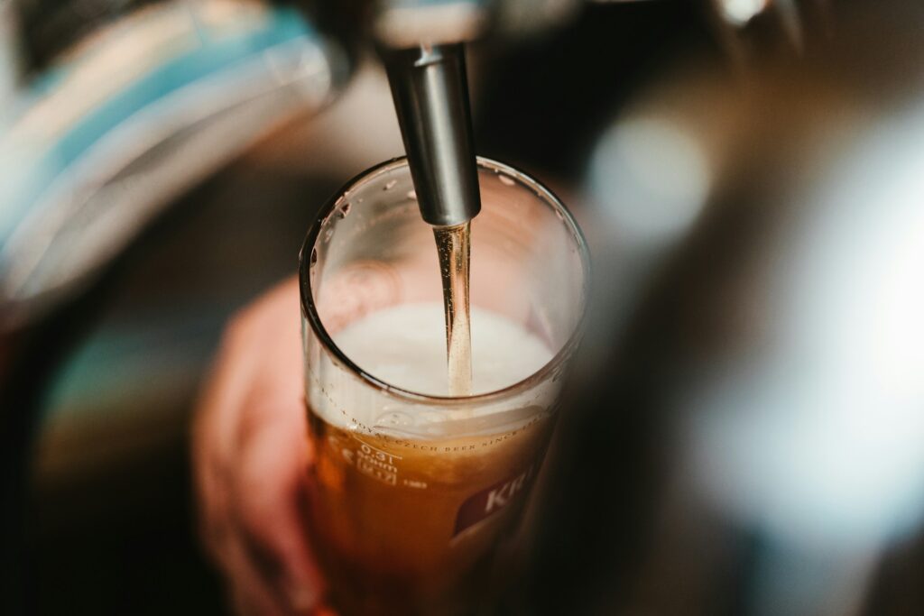 person filling clear glass with beer
