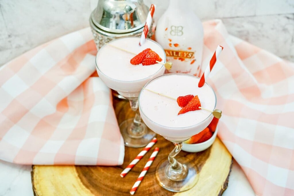 Two completed Strawberry Colada Cocktails with strabwerrys on top and a red and white straw sticking out. 