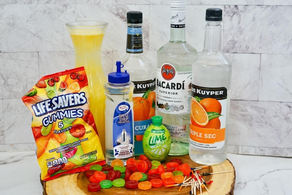 Ingredients required to make shooters, bag of lifesaver gummies, bottle of simple syrup, light rum, triple sec, and blue curacao, pineapple juice, and lime juice. 