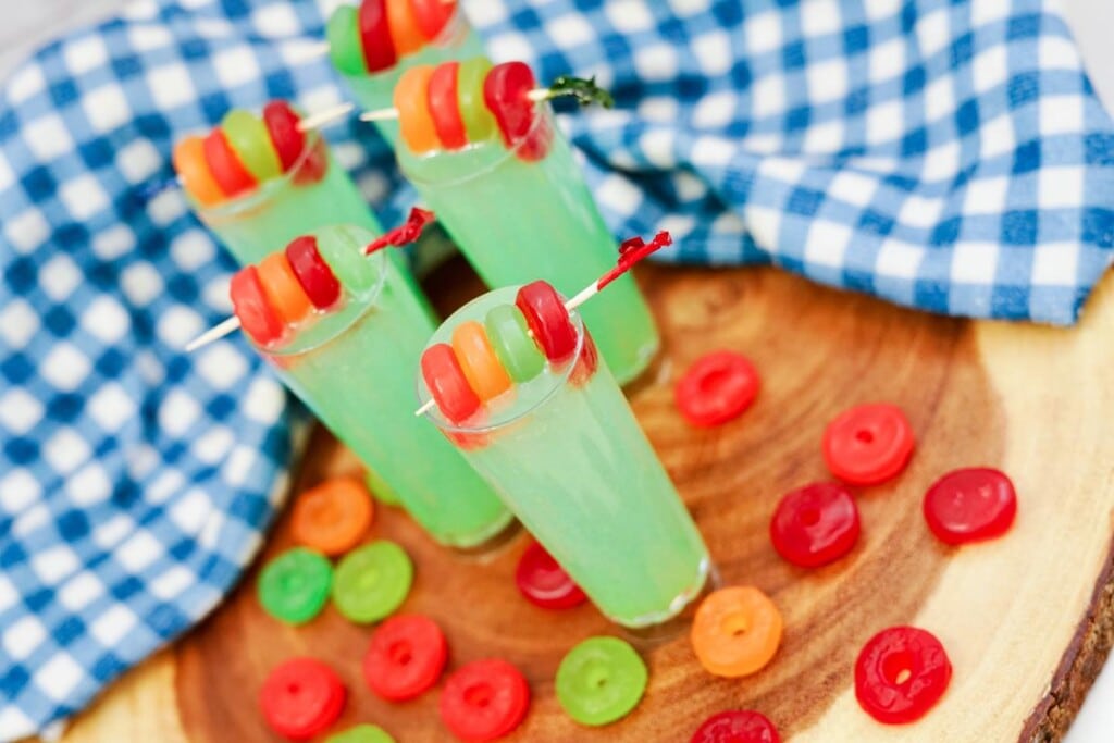 Lifesaver Gummy Shooter Recipe - round wooden board with five completed shooters, all green with four lifesaver gummies on top with many scattered around them. 