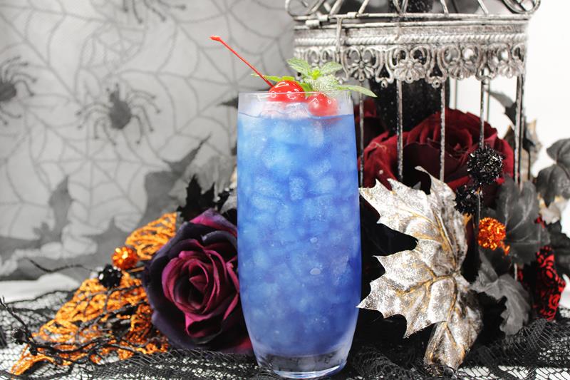 Hocus Pocus cocktail with tequila dark rum and blue curacao in front of a Halloween backdrop