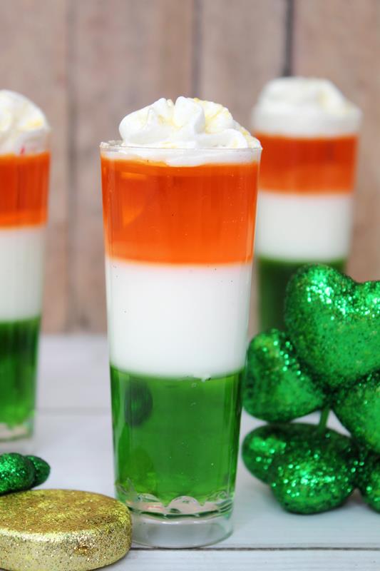 Irish Flag Jello Shots Recipe - Three jello shots, sparkly clover leaves beside it. 
