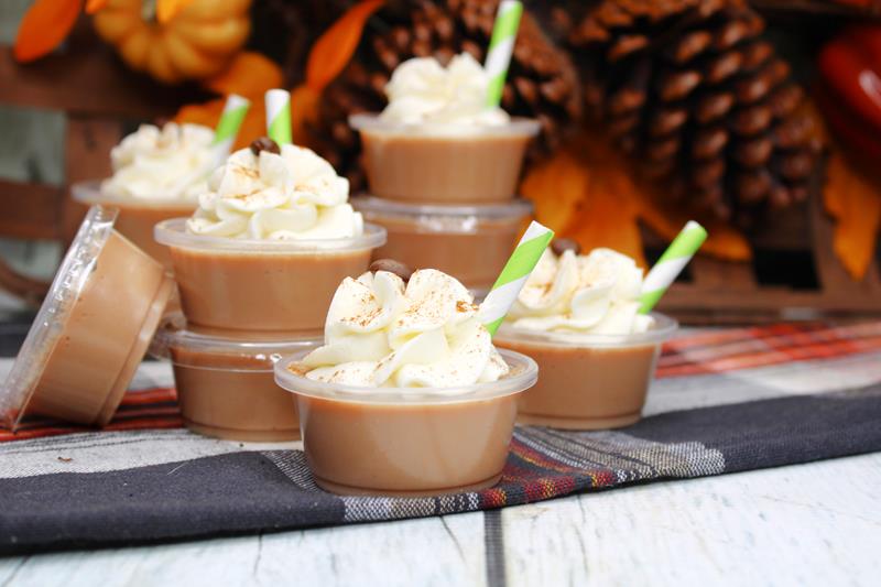 ten pumpkin pie latte jello shots on a table with pinecones and fall leaves in the background. 