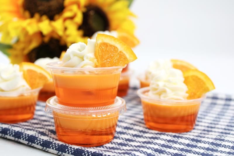 Orange Mango Daiquiri Jello Shots on blue and white table closth with sunflowers in background. 