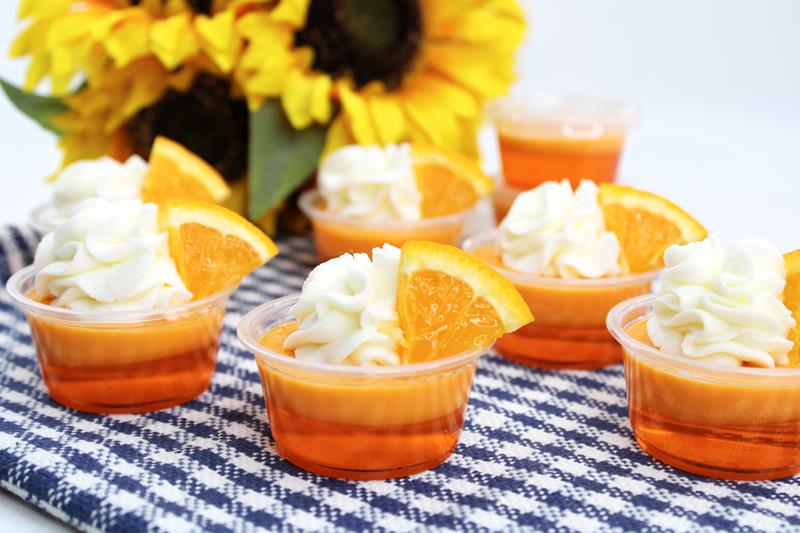 Orange Mango Daiquiri Jello Shots on a blue and white table cloth with sunflowers in the background. 