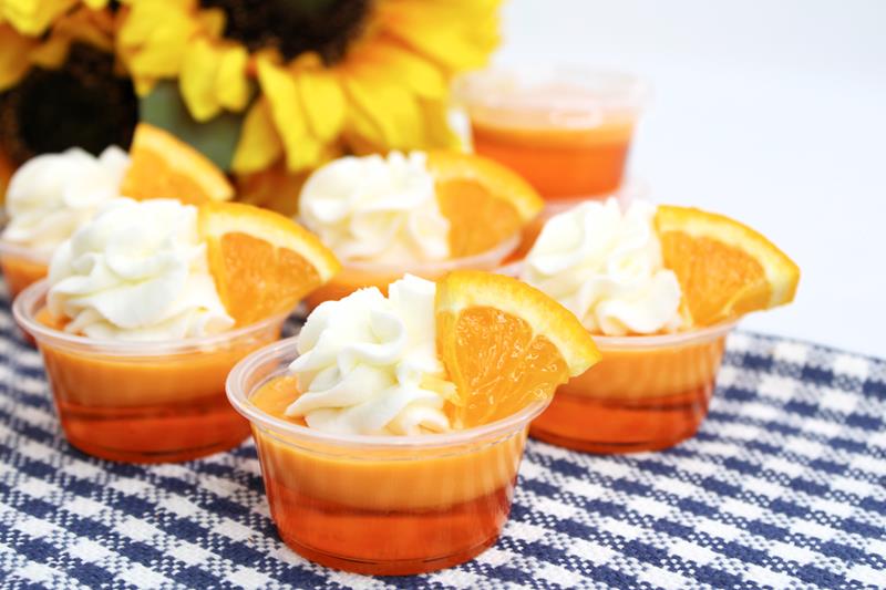 blue and white table cloth with 7 completed jello shots all with whipped cream and orange slices as garnish. 