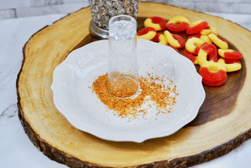 White plate with Tajin seasoning on it with a shooter glass. 