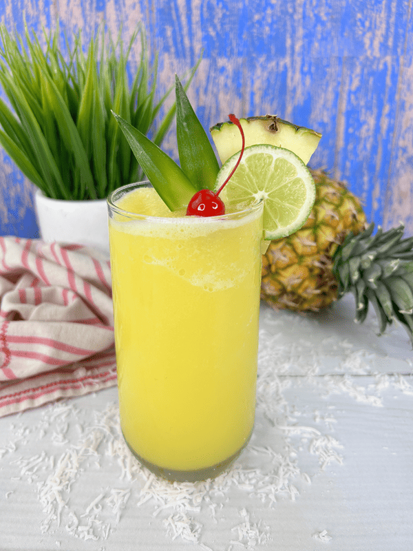 Completed slushy cocktail with full pineapple and a green plant in background. 