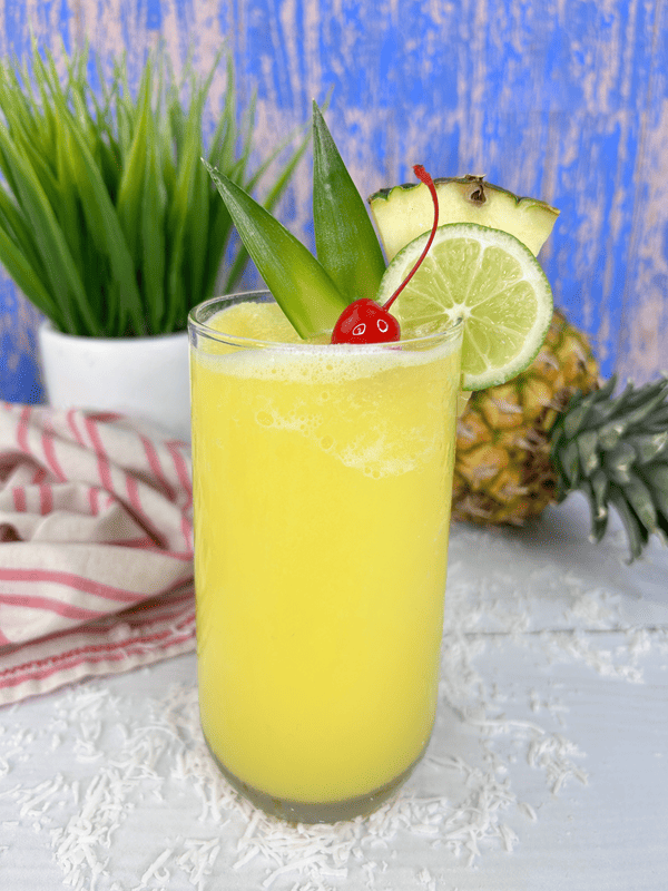 Pineapple Rum Slushy drink with garnishes and pineapple in background. 